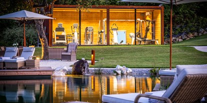 Hüttendorf - Pools: Infinity Pool - Österreich - Fitness-Kubus in der Parkanlage mit Panoramablick auf den Naturschwimmteich. - Golden Hill Country Chalets & Suites