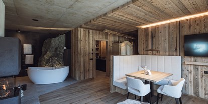 Hüttendorf - Italien - Freistehende Badewanne, Kamin und Essbereich im Landschaftschalet
Im Hintergrund die Steinfelsendusche und die Küche - Amus Chalets Dolomites