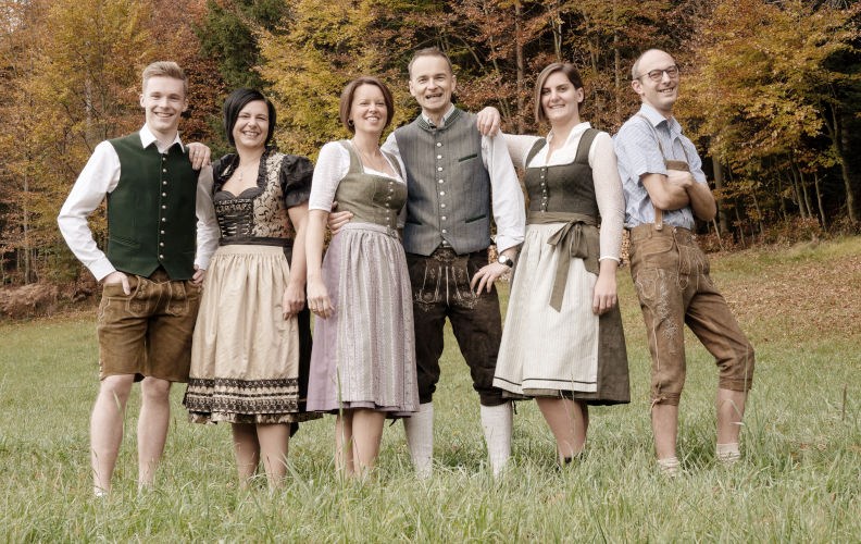 Foto des Teams von Chaletdorf.info in traditioneller Kleidung am Waldrand