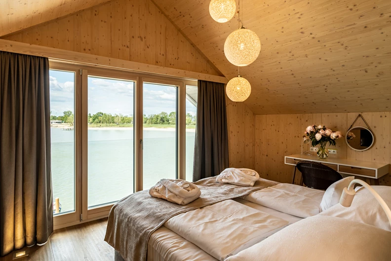Schlafzimmer mit gro&szlig;em Fenster und Blick auf den See