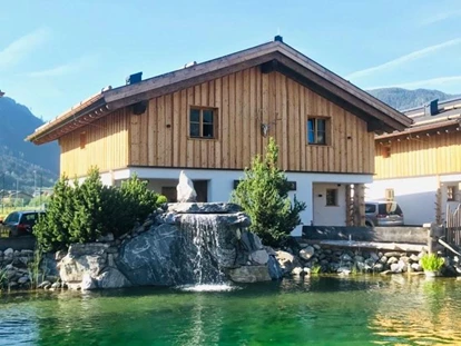 Hüttendorf - Snow Space Salzburg - Flachau - Wagrain - St. Johann - Eines unserer Chalet Hütten mit unserem Naturschwimmteich davor.  - Sieglhub Chalets Appartements Hotel