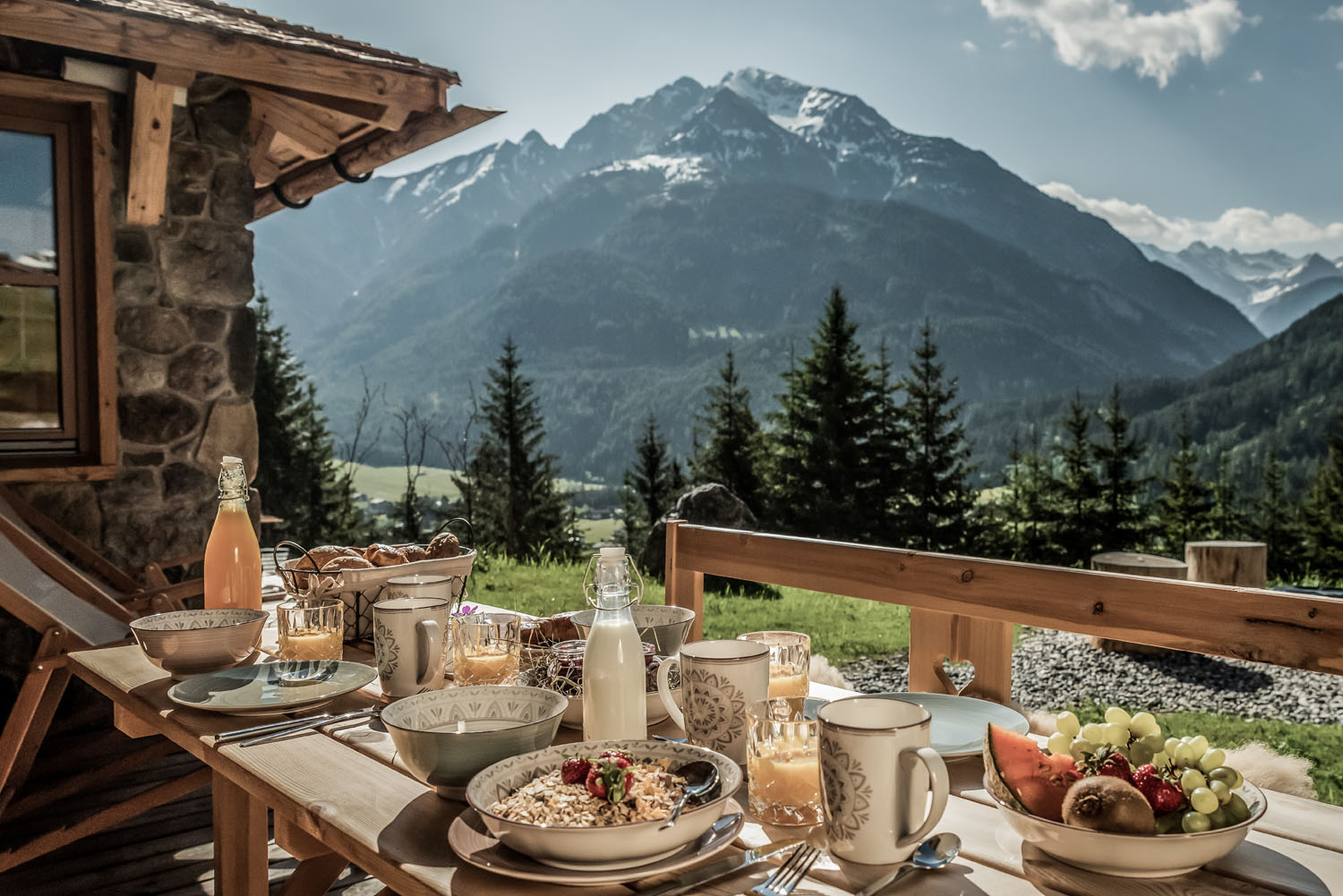 Hüttendorf - Frühstück: Frühstückservice - Almfrühstück auf der Terrasse im Berg-Chalet. Ein echtes Highlight im Benglerwald Berg Chaletdorf ist das liebevoll zubereitete Almfrühstück, das direkt ans Chalet geliefert wird – mit regionalen Spezialitäten, frischen Zutaten und herrlichem Ausblick auf die Lechtaler Alpen. - Benglerwald Berg Chaletdorf