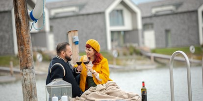 Hüttendorf - Schwerpunkt: Romantikurlaub - Pärchen auf Steg mit Picknick, Hintergrund Residenzen am See - lakeside - VILA VITA Pannonia