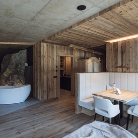 Chalet: Freistehende Badewanne, Kamin und Essbereich im Landschaftschalet
Im Hintergrund die Steinfelsendusche und die Küche - Amus Chalets Dolomites