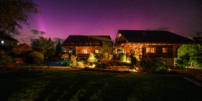 Hüttendorf - Parkplatz direkt an der Hütte - Außenansicht der Chalets Morgensonne und Abendrot bei Nacht mit Polarlichtern - Heumanns Blockhäuser am Wald